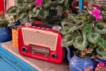 KRotes Retroradio auf einem Balkontisch zwischen blühenden Topfpflanzen.